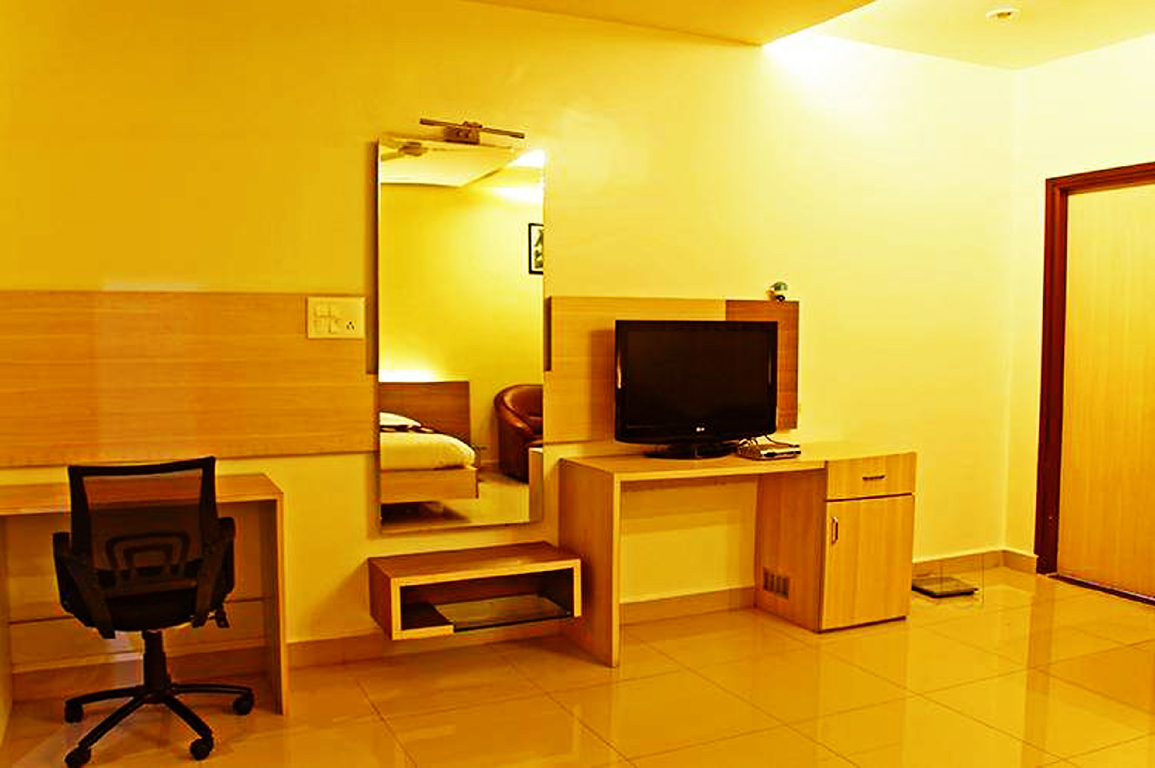 A compact hotel room with a wooden desk, a television, a chair, and a mirror.