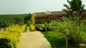 A pathway leading to a building with a tiled roof, surrounded by lush greenery and a body of water.