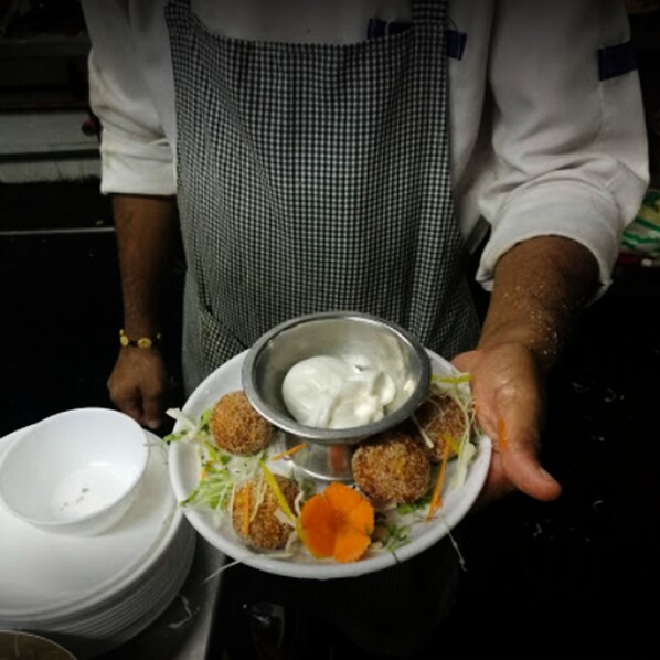 A person holding a plate with food items and a bowl of sauce.