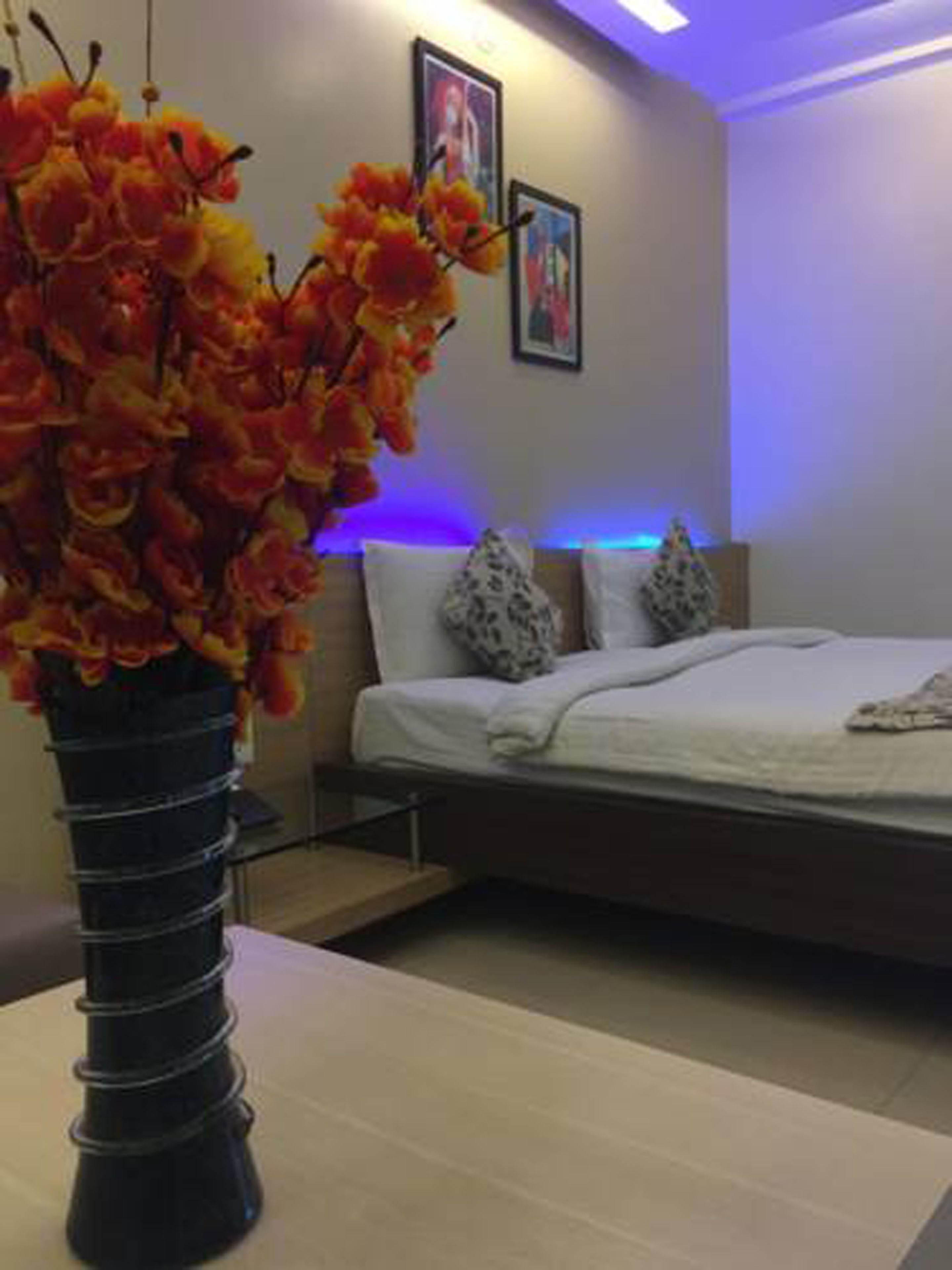 A bedroom with a bed, a nightstand, a vase with flowers, and a wall with two framed pictures.