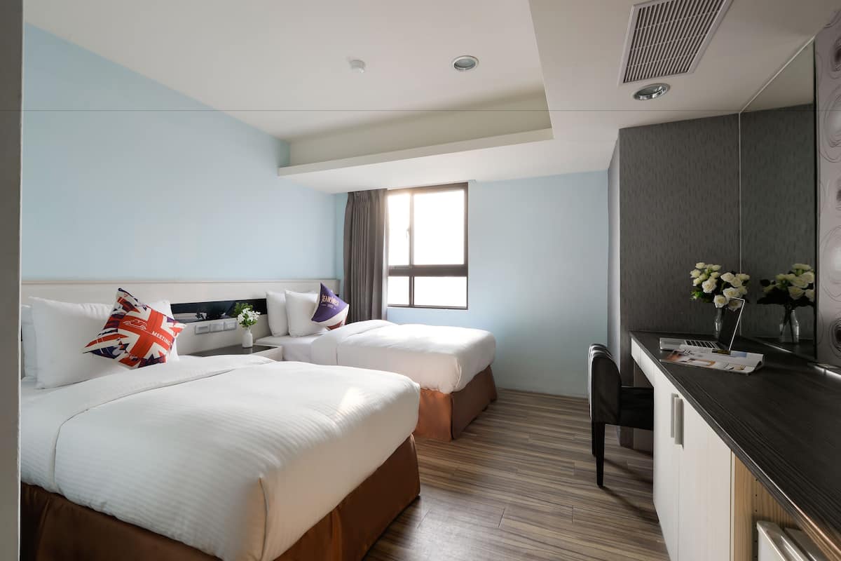 A hotel room with two beds, a desk, and a window.