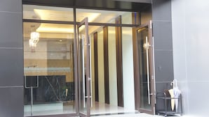 A modern entrance with glass doors, a metal cart with an umbrella, and a chandelier visible through the glass. - Taichung Saint Hotel (Taichung)