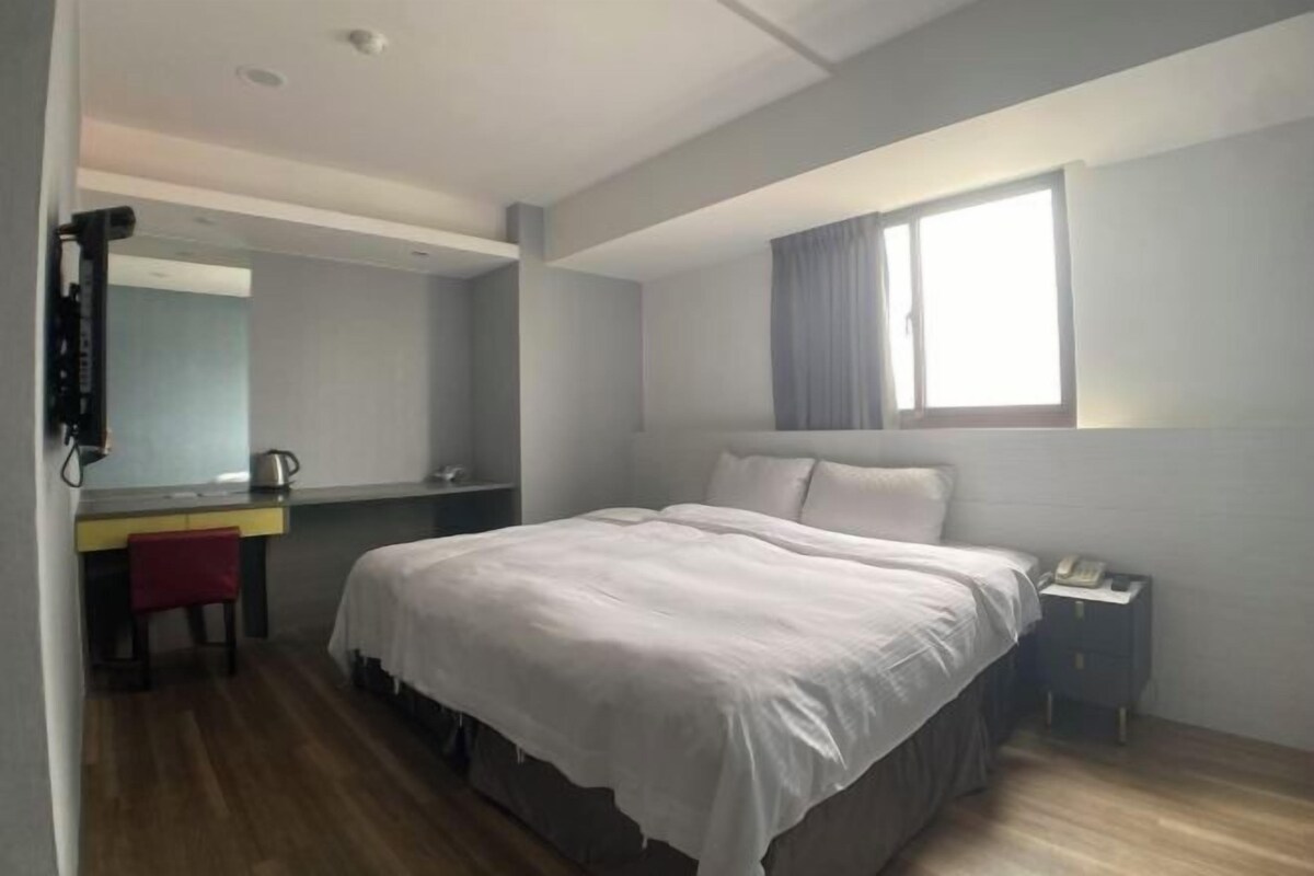 Un dormitorio con cama, escritorio, silla, mesita de noche y ventana.