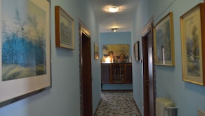 A hallway with framed artwork on the walls, a tiled floor, and a radiator on the right. - B&B Col Moschin (Mestre)