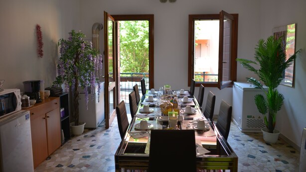 A dining area with a long table set for a meal, potted plants, and a view through open doors. - B&B Col Moschin (Mestre)
