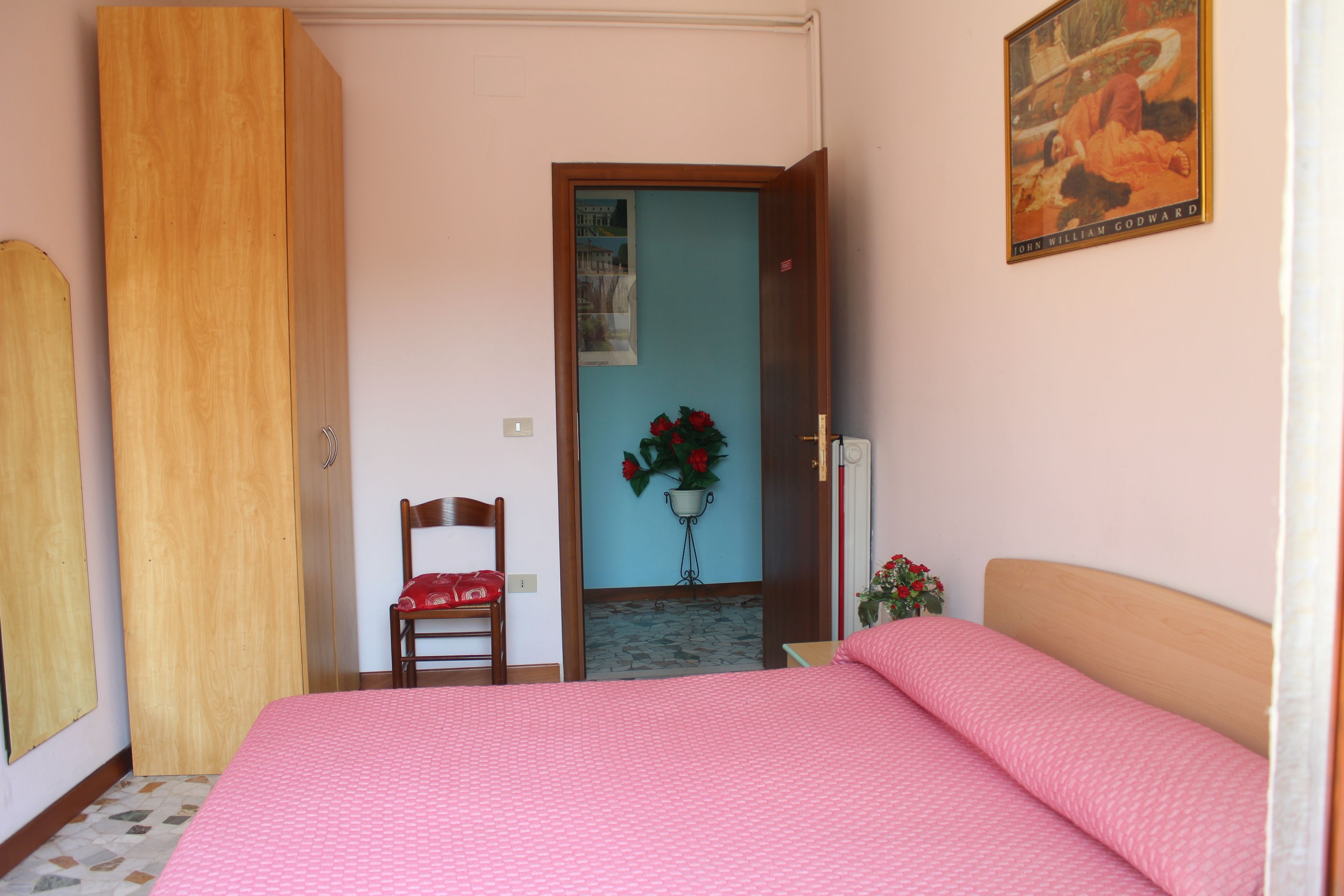A bedroom with a bed, a wooden wardrobe, a chair, a wall-mounted flower pot, and a poster.