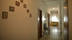 A hallway with framed pictures on the wall, a lamp, and a bed with a yellow blanket in the distance. - B&B Col Moschin (Mestre)