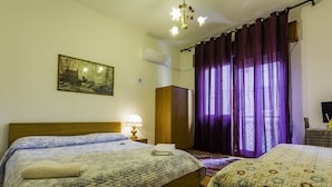 A hotel room with two beds, a wooden headboard, a nightstand with a lamp, a painting on the wall, and purple curtains. - B&B Col Moschin (Mestre)