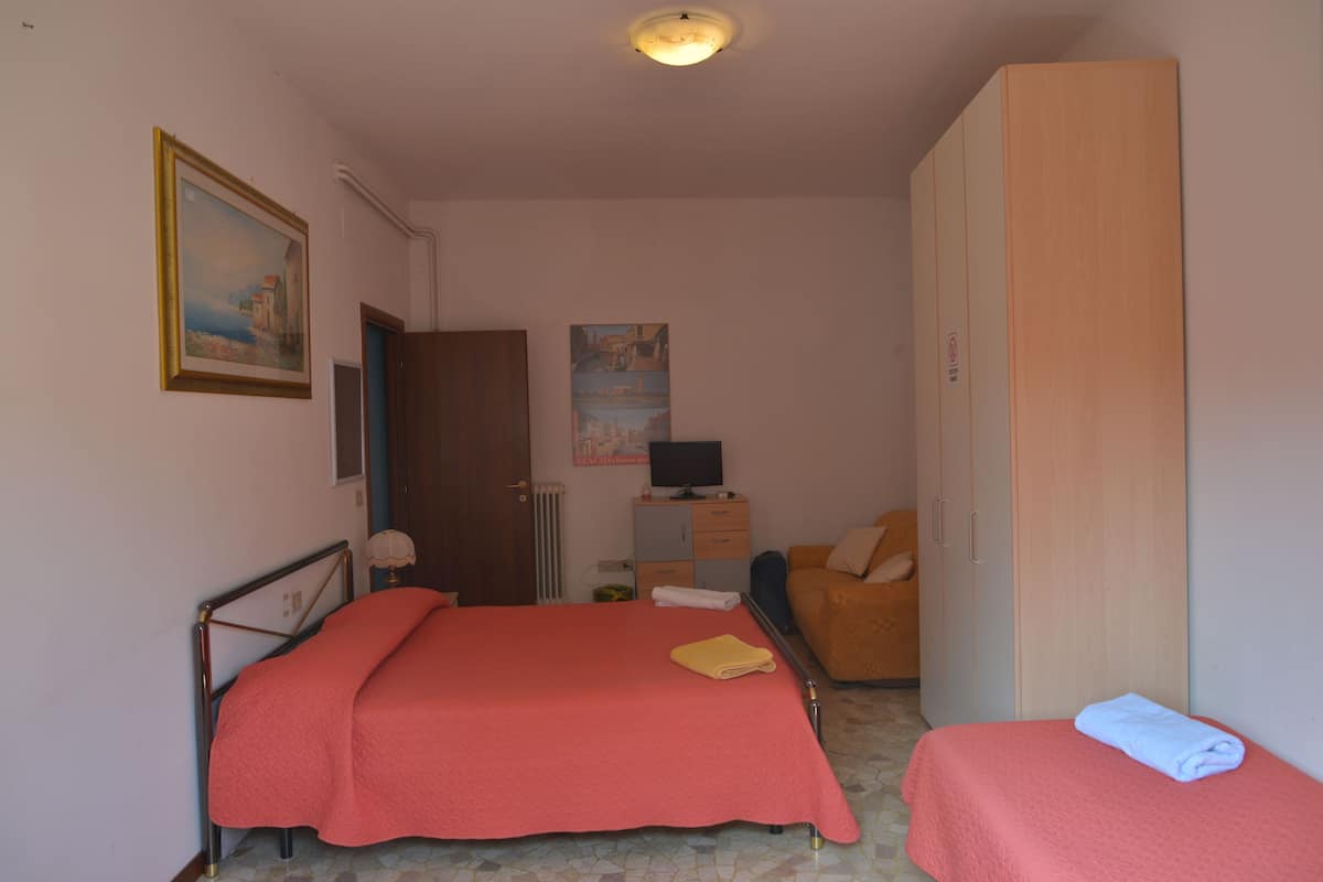 A bedroom with a bed, a bedside table, a chair, a wardrobe, and a painting on the wall.