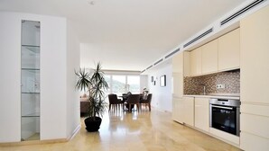 A modern kitchen with a built-in oven, a dining area with a table and chairs, and a large potted plant.