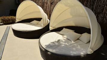 Deux fauteuils de jardin en osier, dotés de coussins blancs et de toiles de protection, sont placés sur une terrasse carrelée.