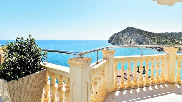 A balcony with a view of the sea and a rocky hill.