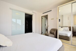 Quarto de hotel com uma cama grande, área de estar, porta de vidro deslizante e um espelho refletindo um quarto.