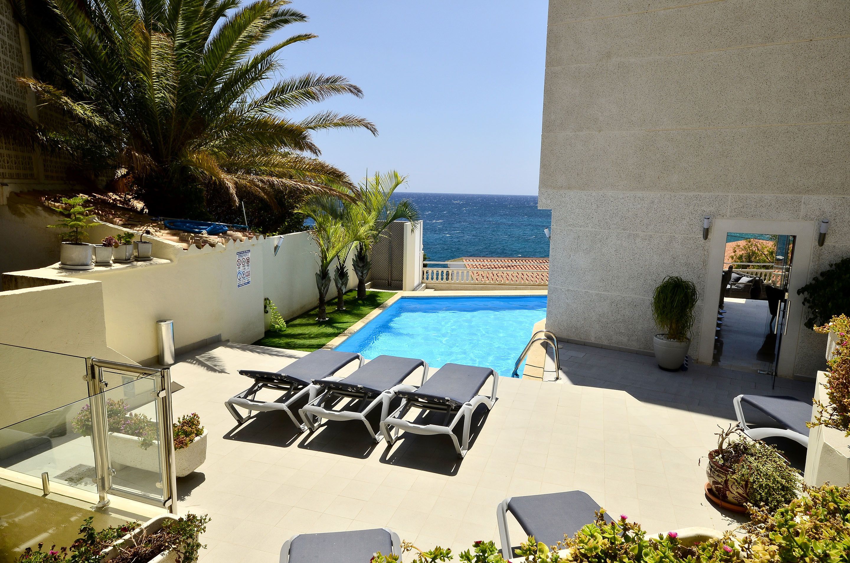 A pool area with lounge chairs and a view of the sea.