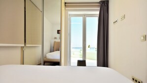 A hotel room with a bed, a chair, a sliding door to a balcony, and a view of the outside.