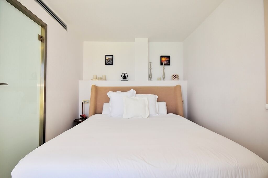 A neatly made bed with white linens, a wooden headboard, and a nightstand with a lamp.