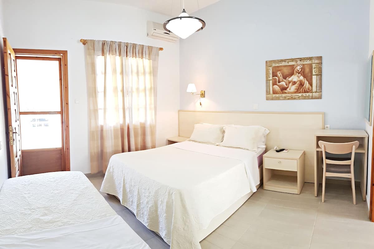 A hotel room with a large bed, a bedside table with a lamp, a desk with a chair, and a painting on the wall.