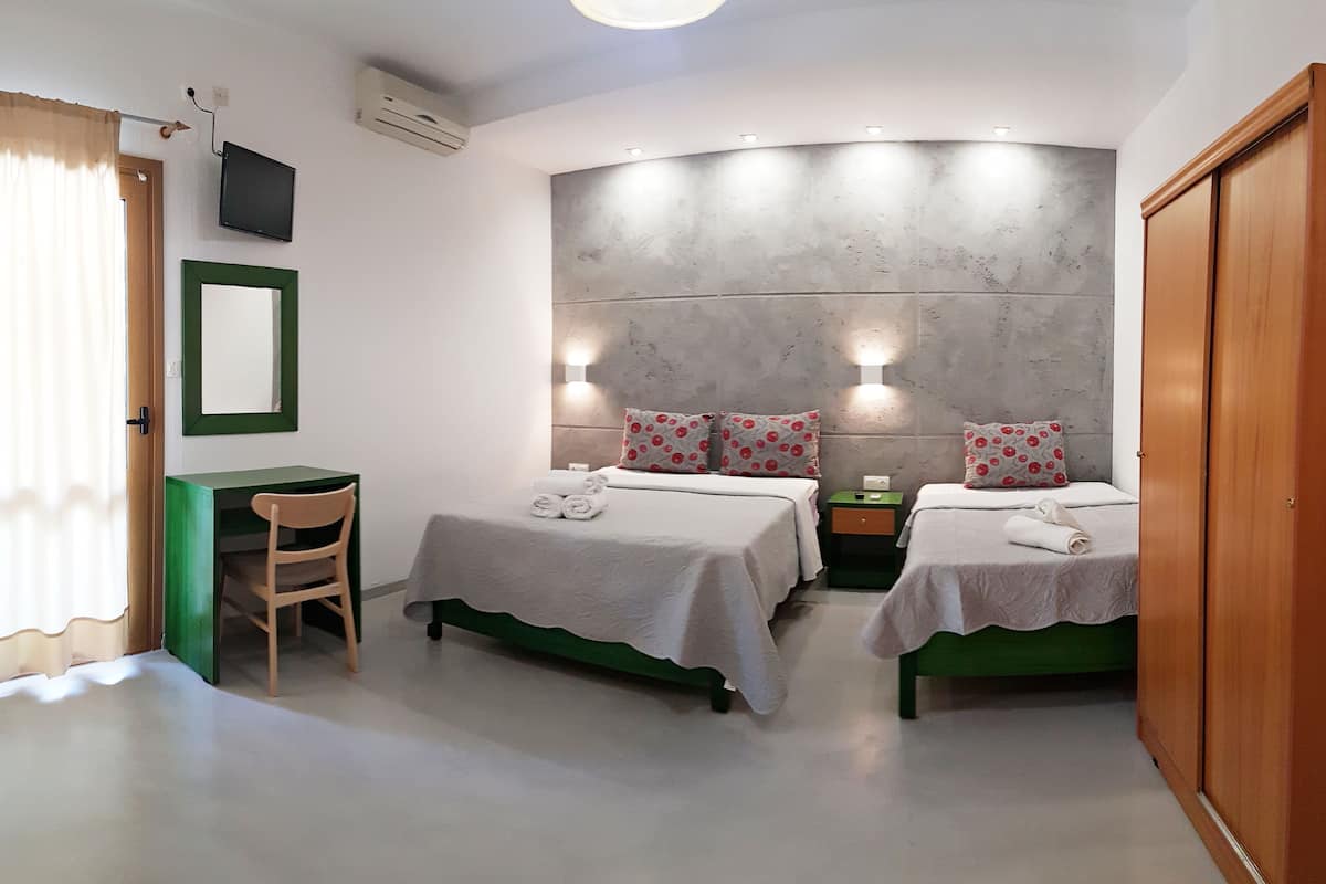 A hotel room with two beds, a desk, a chair, a wardrobe, and a large wall with a built-in light fixture.