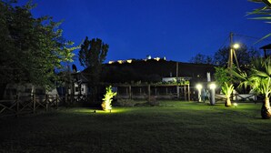 A nighttime view of a building with a thatched roof, surrounded by a wooden fence and palm trees. - Studios & Apartments Efrosini (Dio-Olympos)
