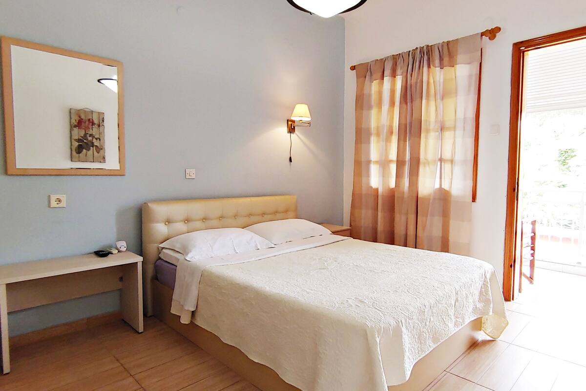 A bedroom with a bed, a bedside table, a lamp, a mirror, and a door leading to a balcony.
