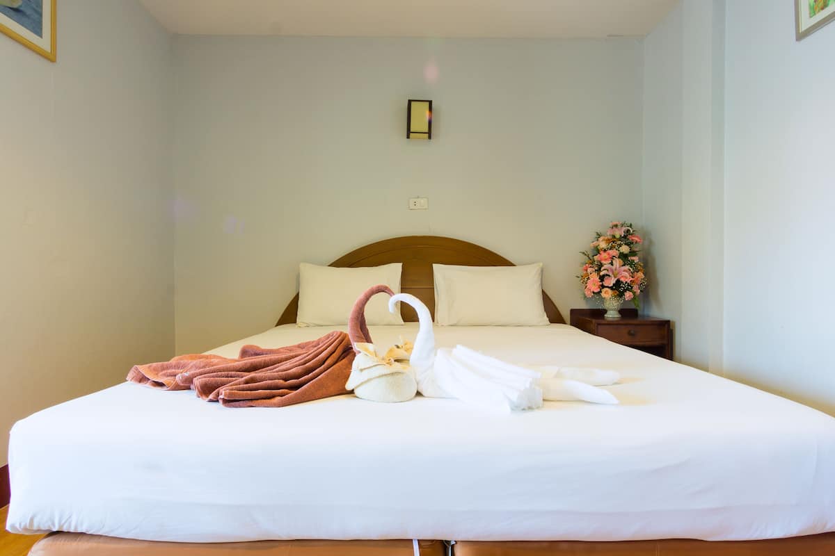 Een net opgemaakt bed met een handdoek in de vorm van een zwaan, een bruine handdoek en een vaas met bloemen op een nachtkastje.