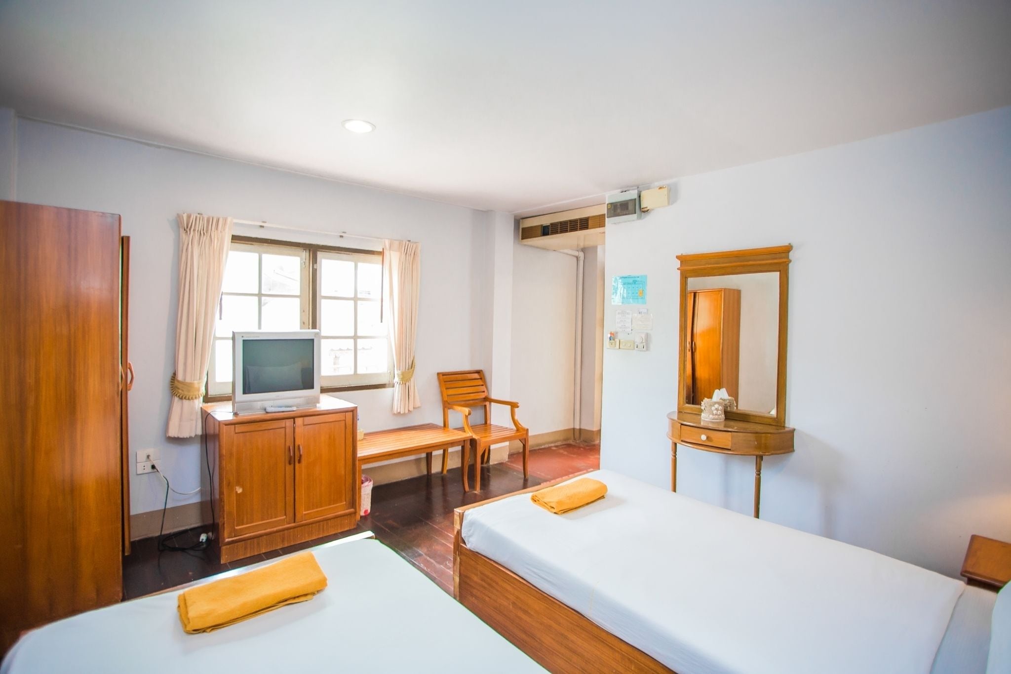A hotel room with two beds, a wooden desk, a television, a chair, a wardrobe, and a mirror.