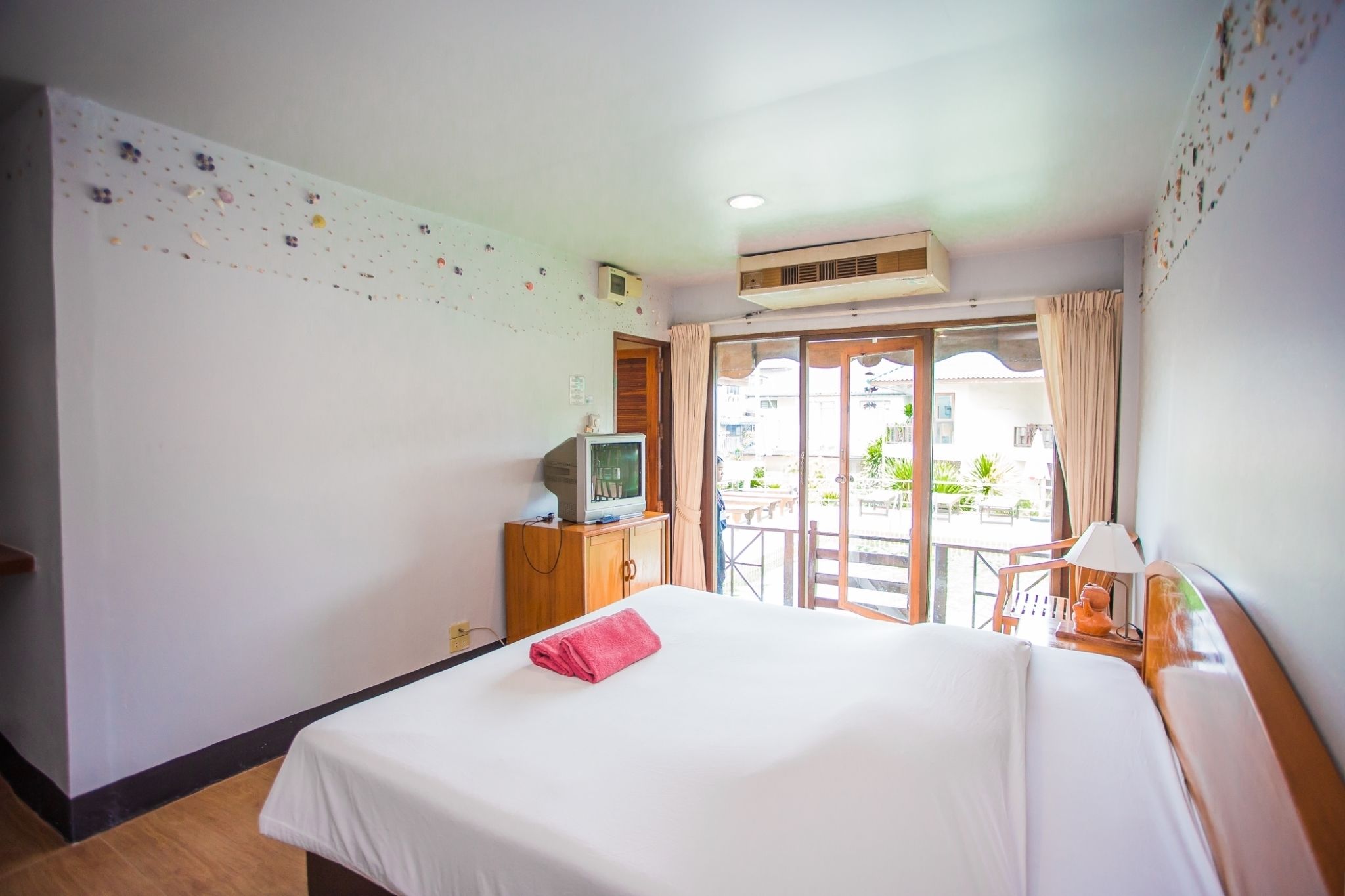 A hotel room with a bed, a television on a wooden cabinet, a balcony with a table and chairs, and a window with curtains.
