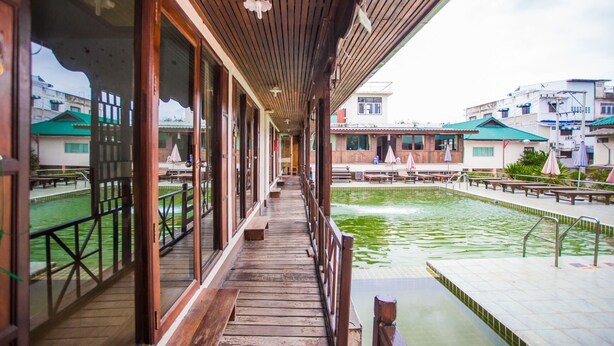 Terraza de madera con bancos que da a una piscina y vistas de edificios.