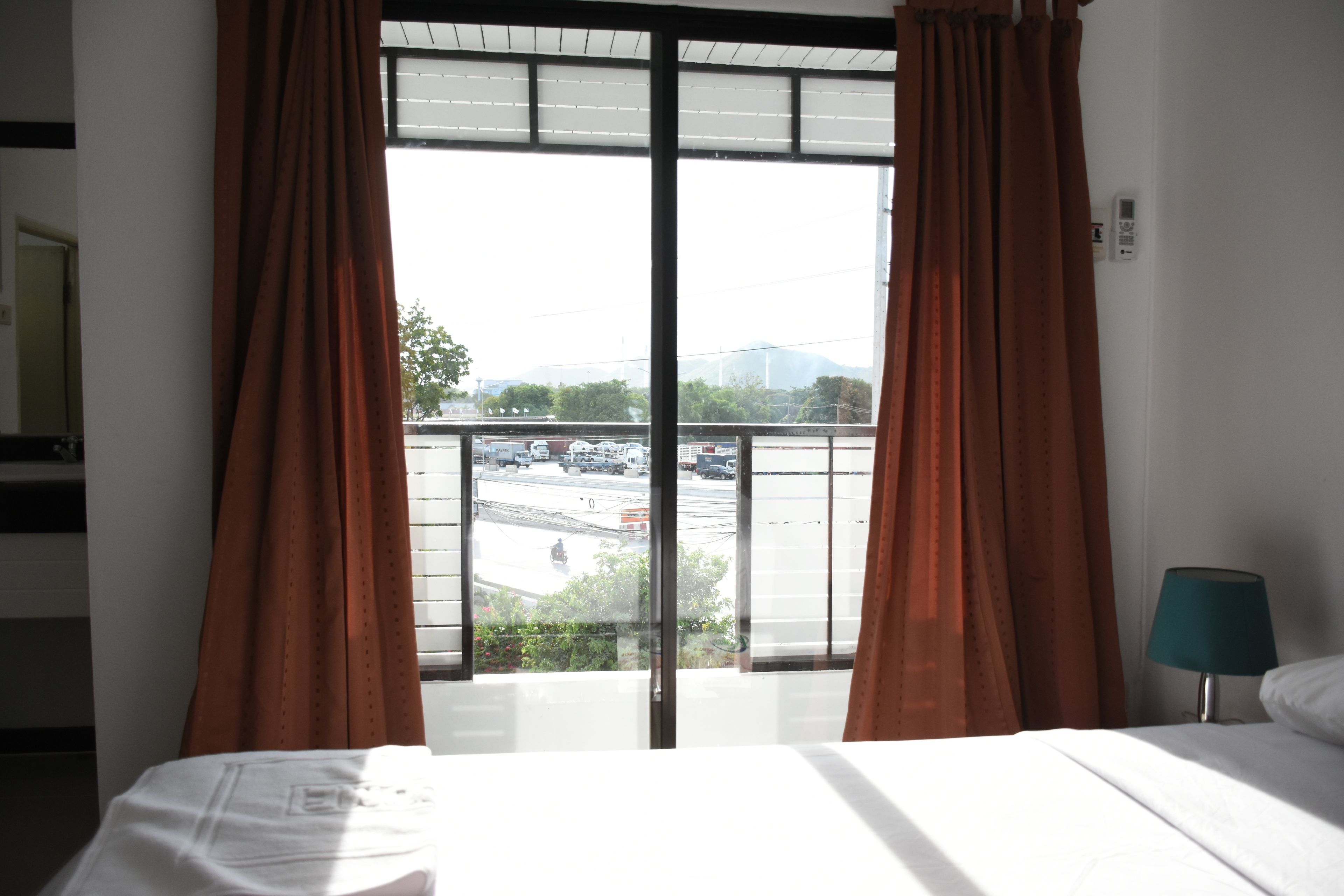 Una habitación de hotel con cama, ventana con cortinas y vistas a un estacionamiento y edificios.