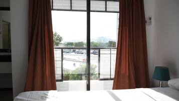 Una habitación de hotel con cama, ventana con cortinas y vistas a un estacionamiento y edificios.