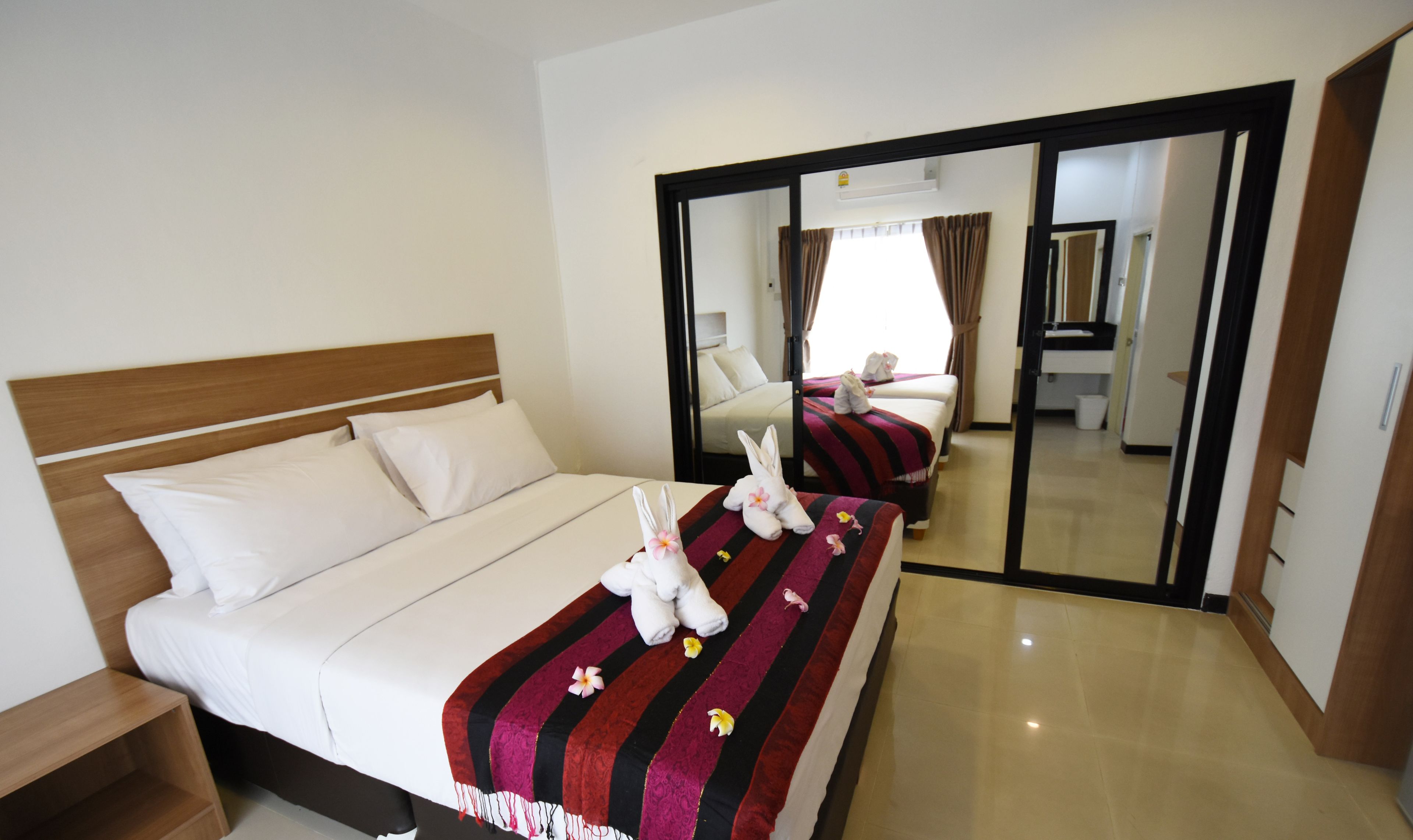 A hotel room with a bed, a nightstand, a mirror, and a bathroom visible through an open door.