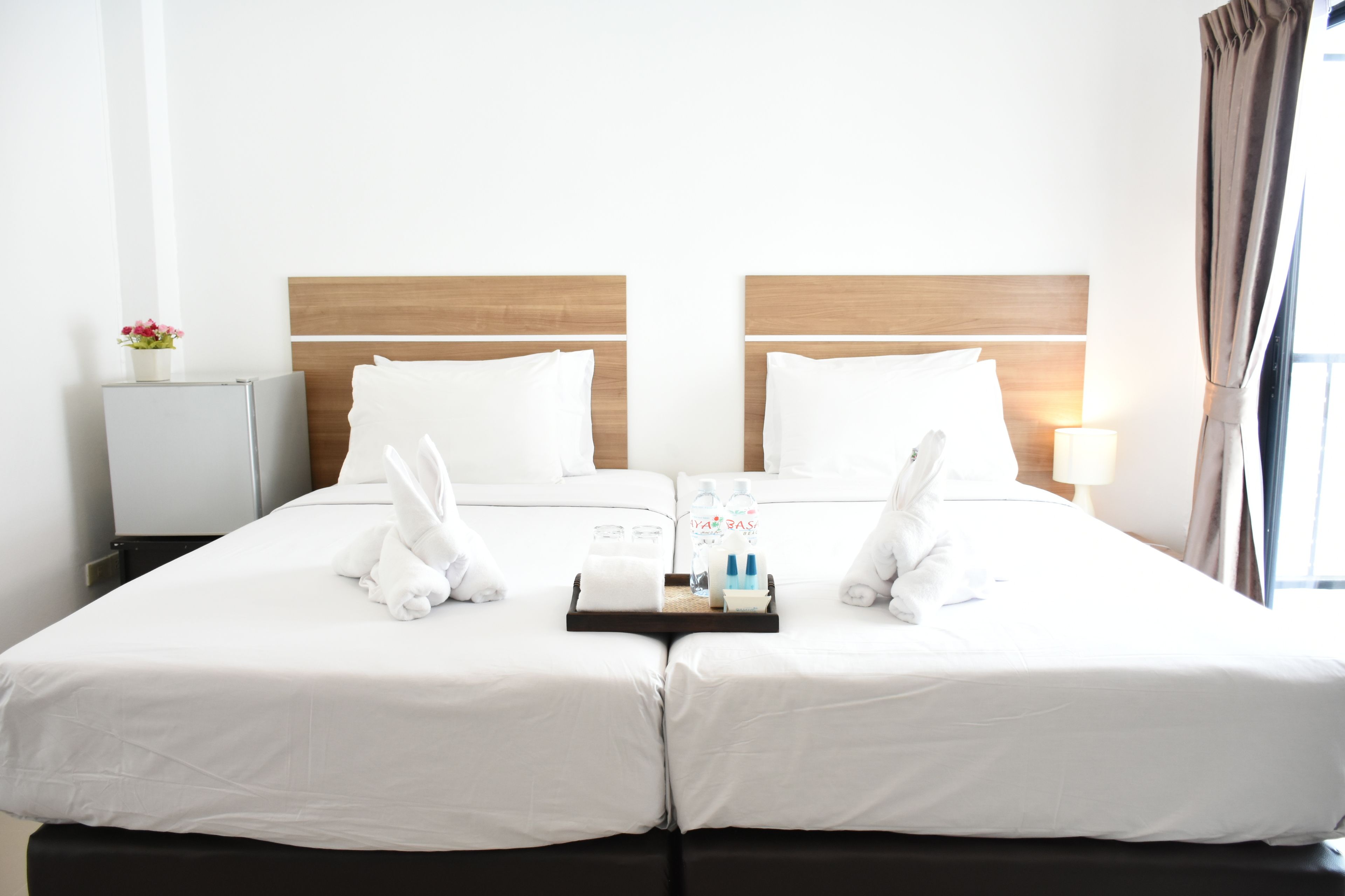 Habitación de hotel con dos camas, una mesita de noche, una lámpara y un ventanal con cortinas.