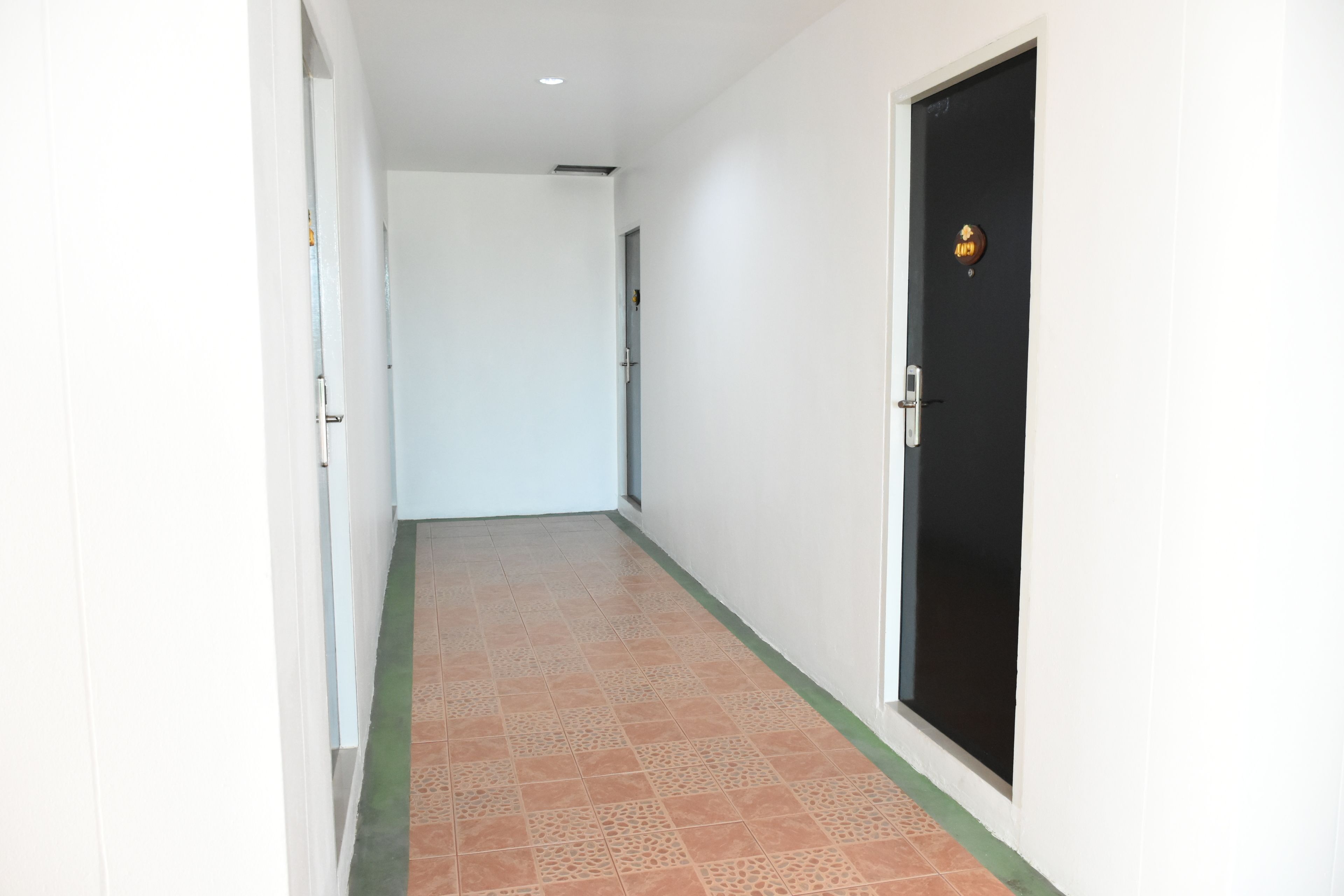 Un pasillo con piso de baldosas, una puerta negra con un emblema dorado y paredes blancas.