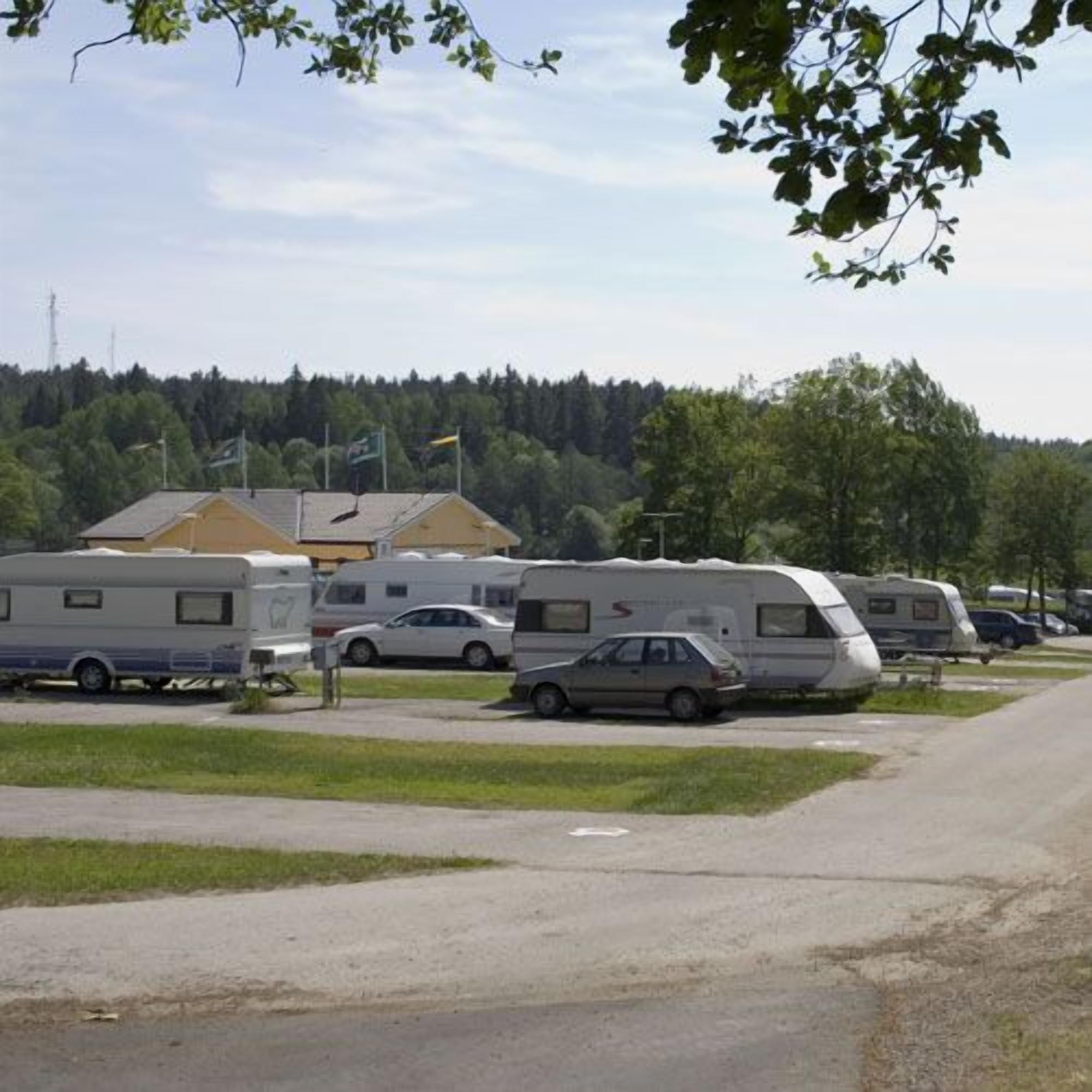 Ein Parkplatz mit Wohnmobilen und Autos, eine Rasenfläche und Gebäude im Hintergrund.