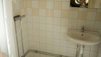 Un baño con lavamanos blanco, ducha y piso de baldosas.