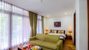 A hotel room with a bed, a green sofa, a small table with a plate of food, and a painting on the wall. - Valley Mountain Hotel (Ho Chi Minh City)