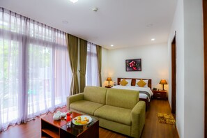 Hotellihuone, jossa on sänky, vihreä sohva, pieni pöytä, jonka päällä on lautanen ruokaa, ja seinällä taulu.
