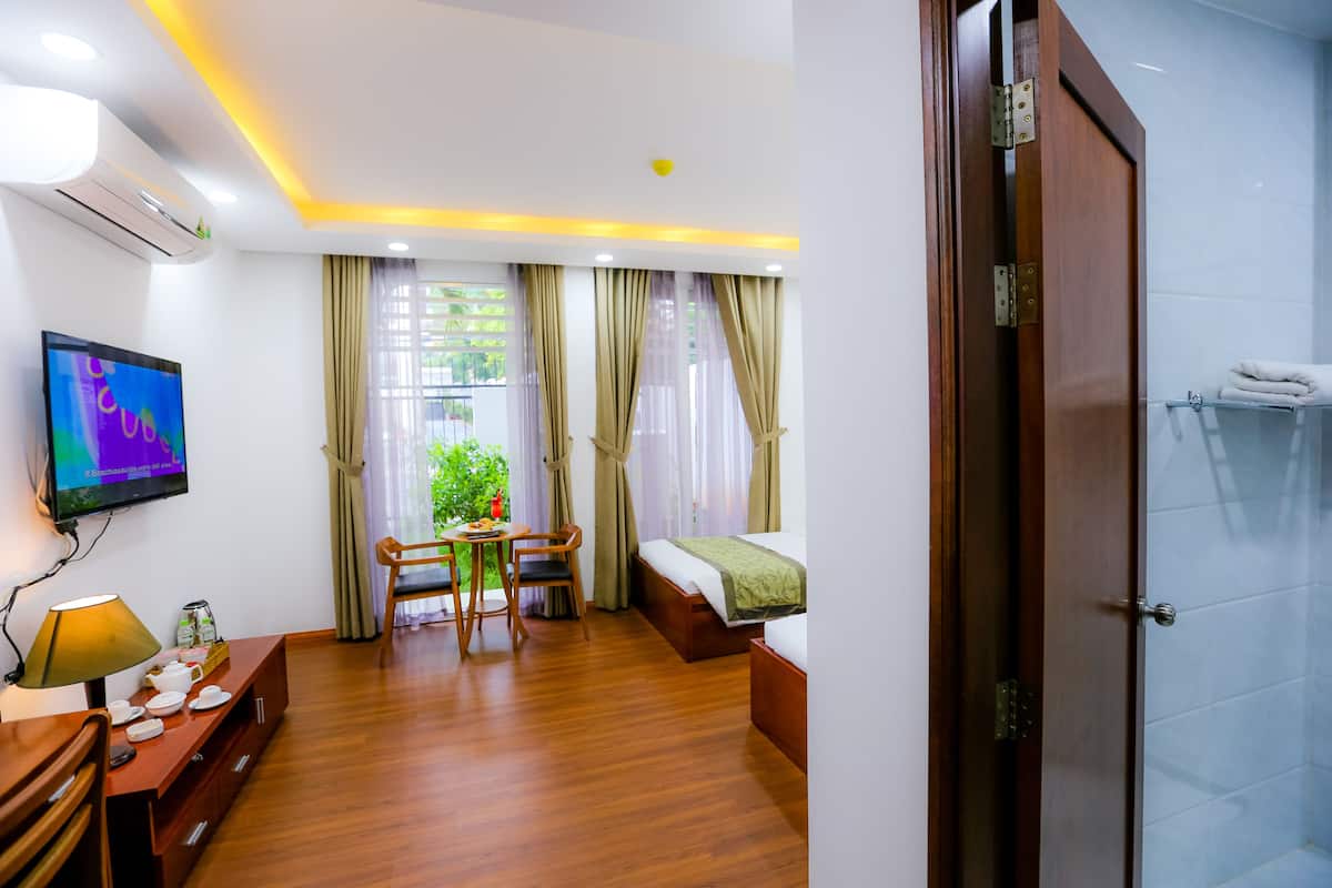 A hotel room with a bed, a desk with a chair, a TV, and a shower area.