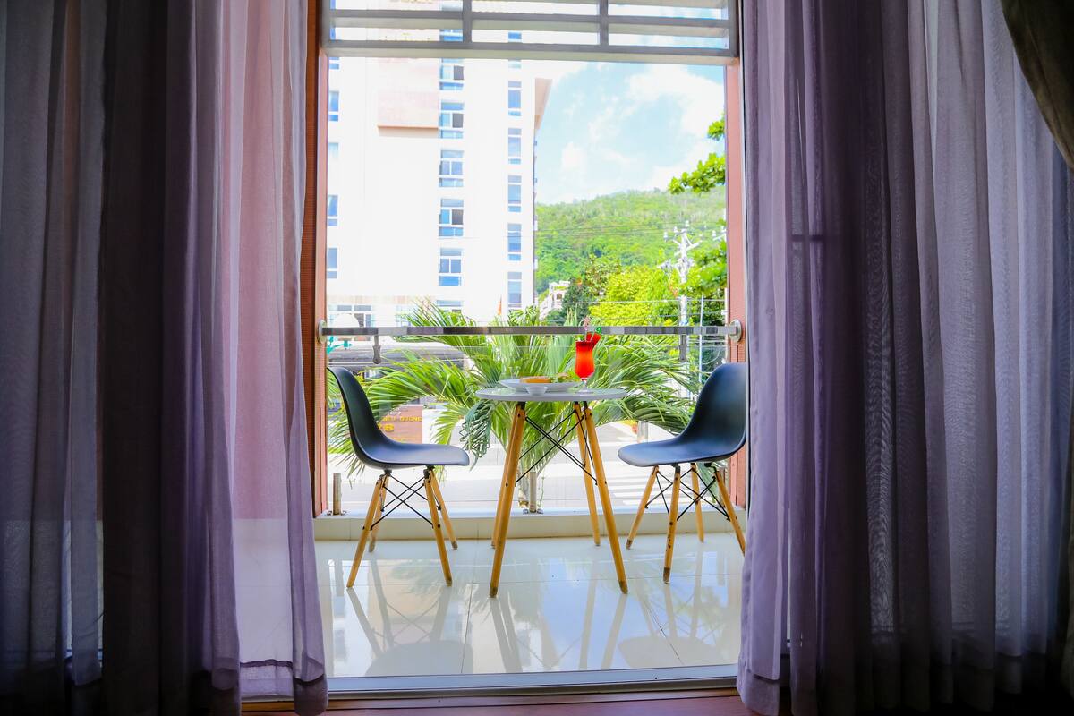 A balcony with a table and chairs, a view of a building, and a red object on the table.