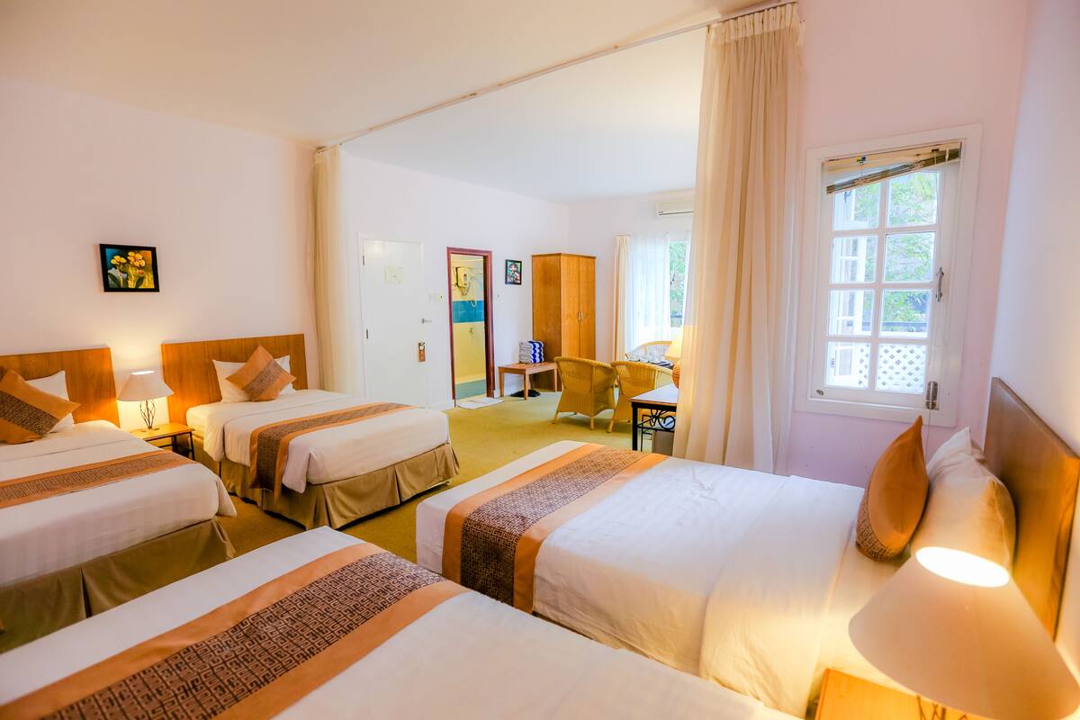 A hotel room with three beds, a desk, and a chair.