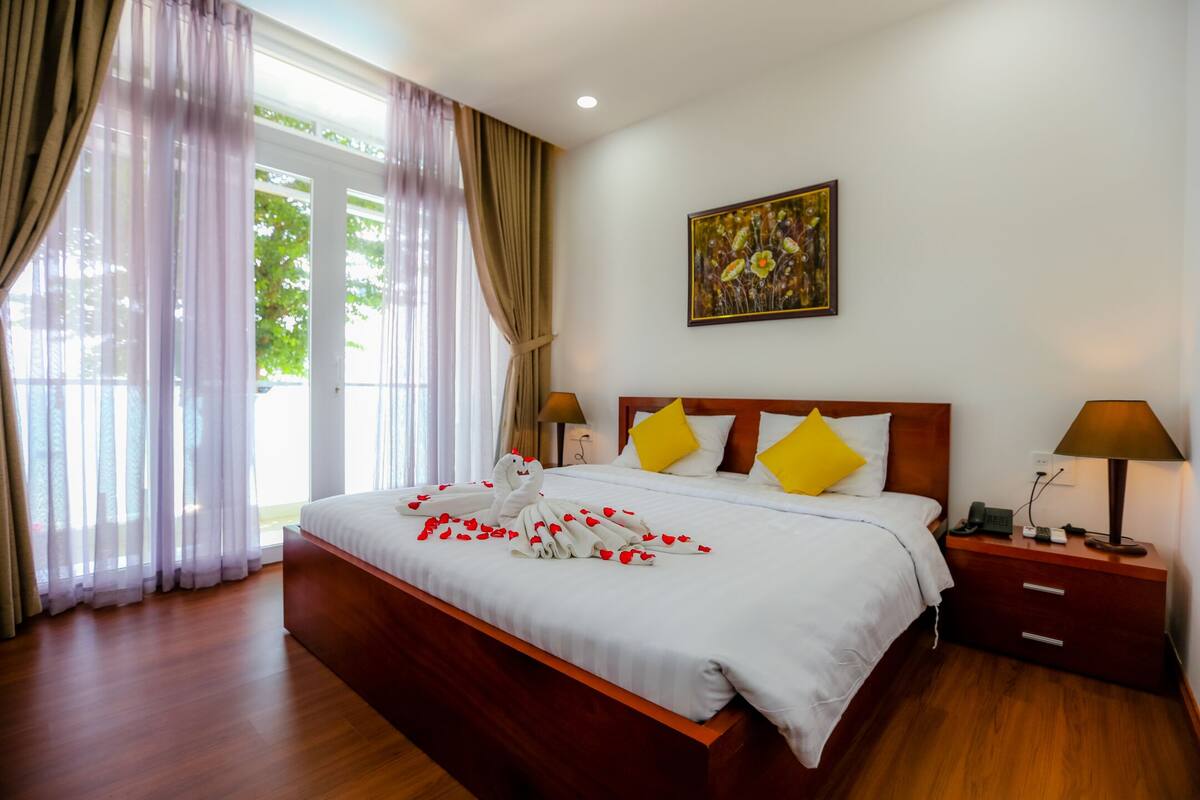 A neatly made bed with a white comforter, two yellow pillows, and a wooden headboard.