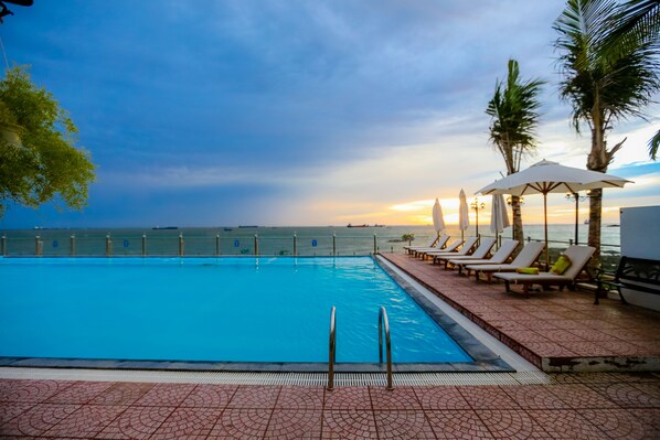 Una piscina con vista al mar, sillas de descanso y palmeras.