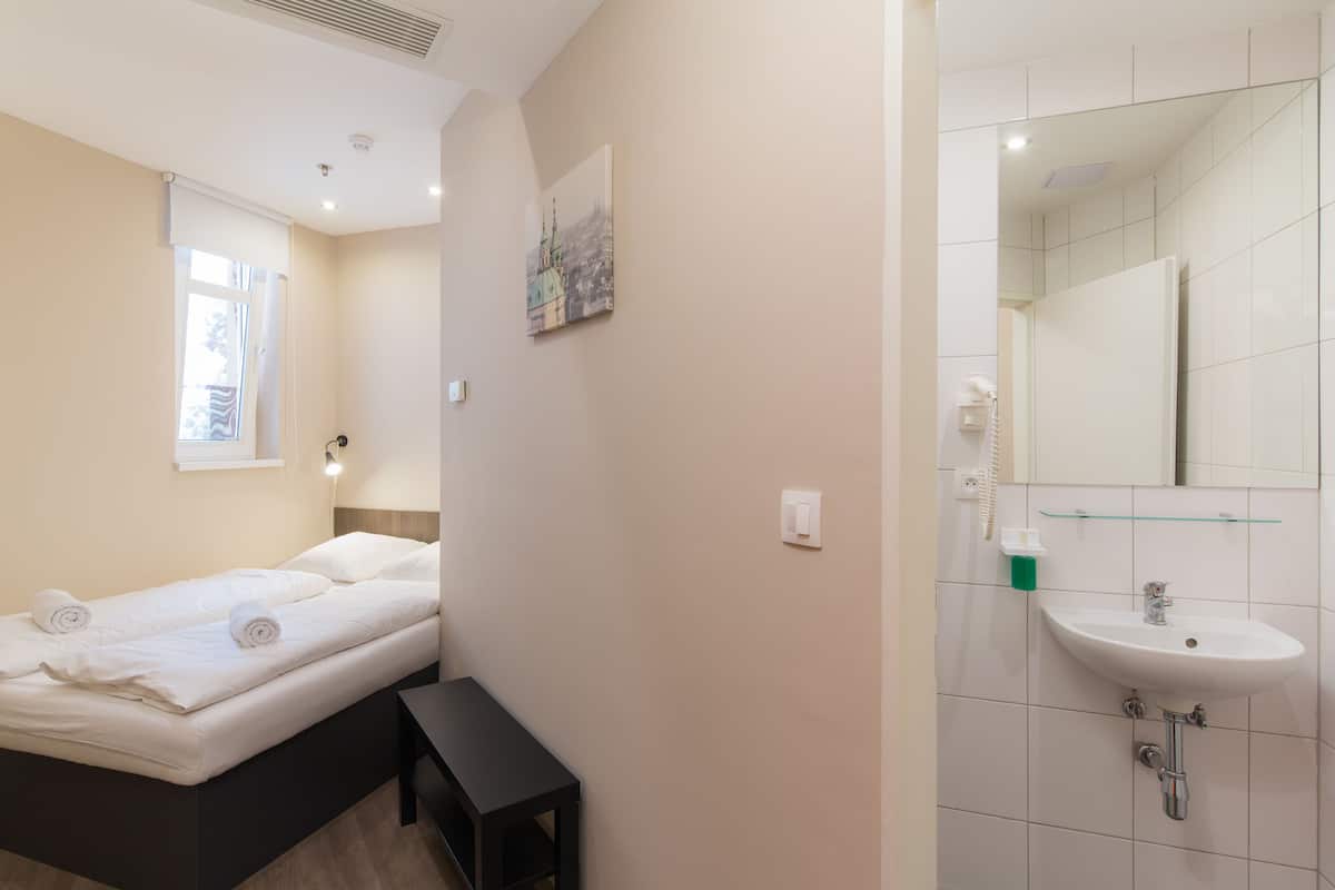 A hotel room with a bed, a small table, a bathroom with a sink and mirror.