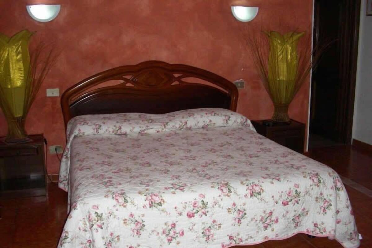 Un dormitorio con cama de madera, ropa de cama floral y dos lámparas fijadas a la pared.