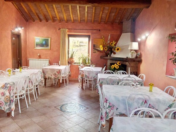 A dining area with multiple tables, chairs, a fireplace, and a window with curtains. - Agriturismo Da Paola (Manciano)
