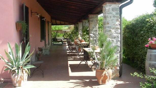 A covered outdoor seating area with stone pillars, tables, and chairs, surrounded by potted plants and a hedge. - Agriturismo Da Paola (Manciano)