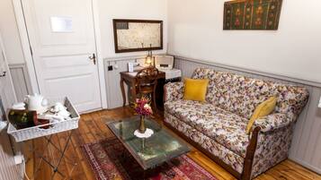 A cozy living room with a floral sofa, a small table, a wicker basket, and a vintage radio.