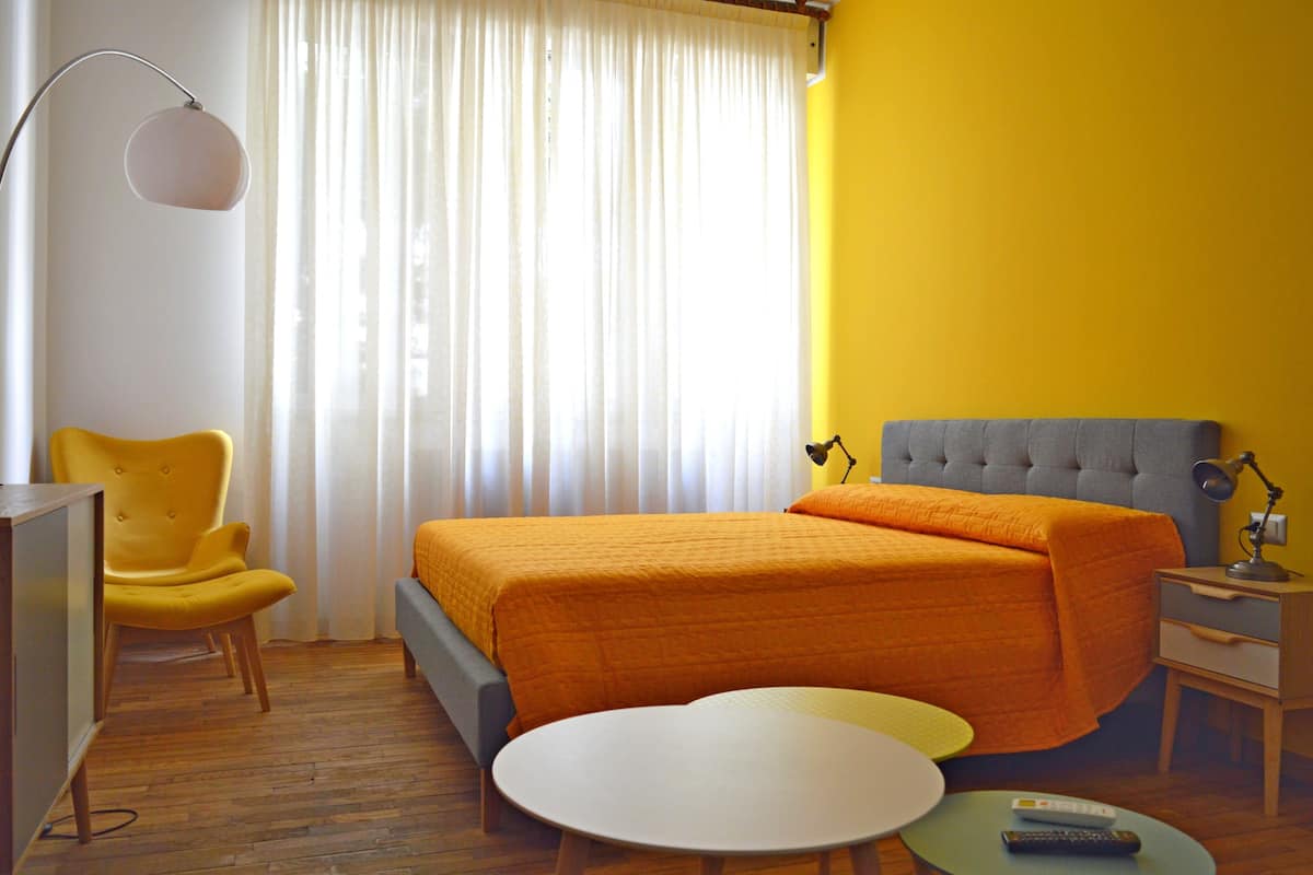 A hotel room with a bed, a chair, a desk, a lamp, and a round table.