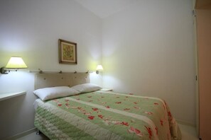 A bedroom with a bed, two bedside lamps, a wall-mounted picture, and a door.