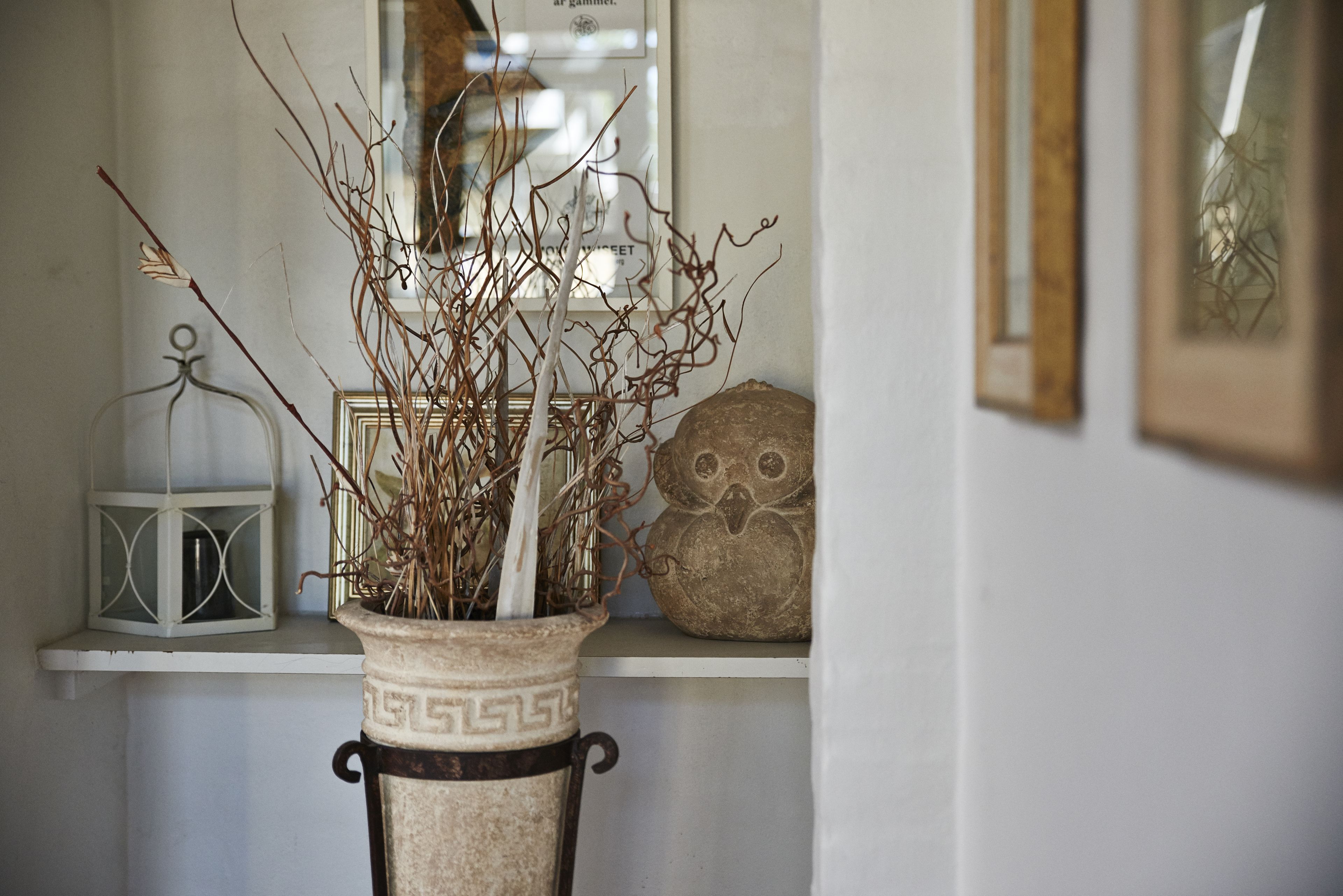 A white vase with a geometric pattern on a pedestal, containing branches and a white candle.
